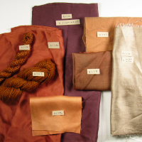 a stack of silk fabrics and yarns in shades of reds, browns, and purples