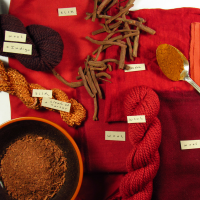 madder root in different forms on a pile of deep red fabrics and yarns