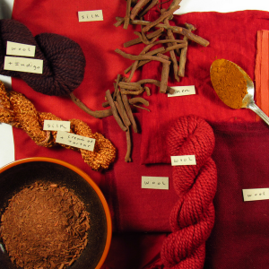 madder root in different forms on a pile of deep red fabrics and yarns