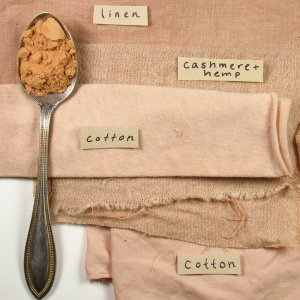 A spoon of tan powder on a stack of pink fabrics and yarn