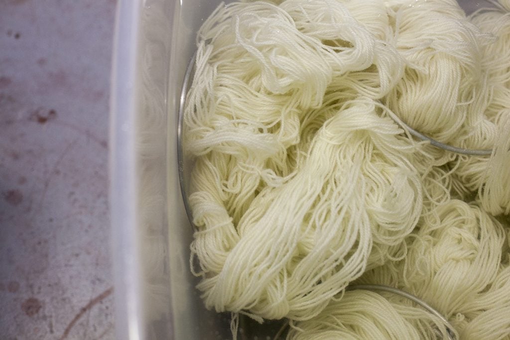 Skeins of undyed yarn on dye rings in a mordant bath