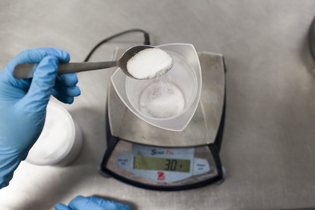 Overhead shot of a gloved hand measuring a white powder over a scale