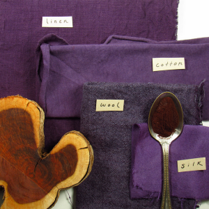 a slice of wood and a spoon of deep red powder on bright purple fabrics