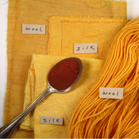 A spoon of red powder on a stack of bright yellow fabrics and yarn