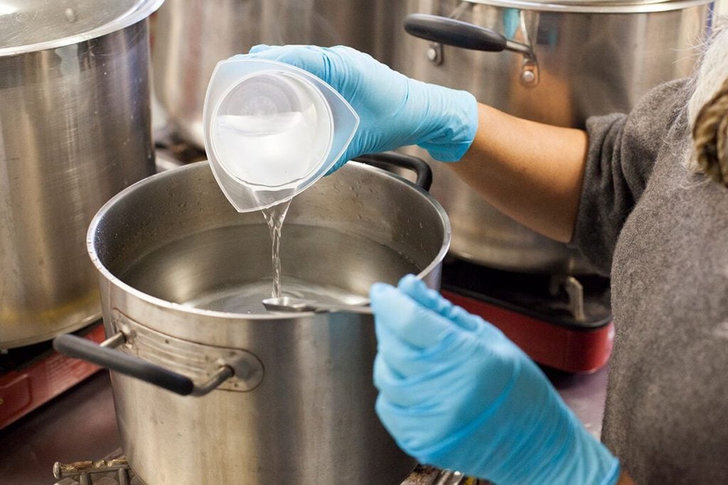Pouring a clear liquid from a plastic beaker into a metal pot