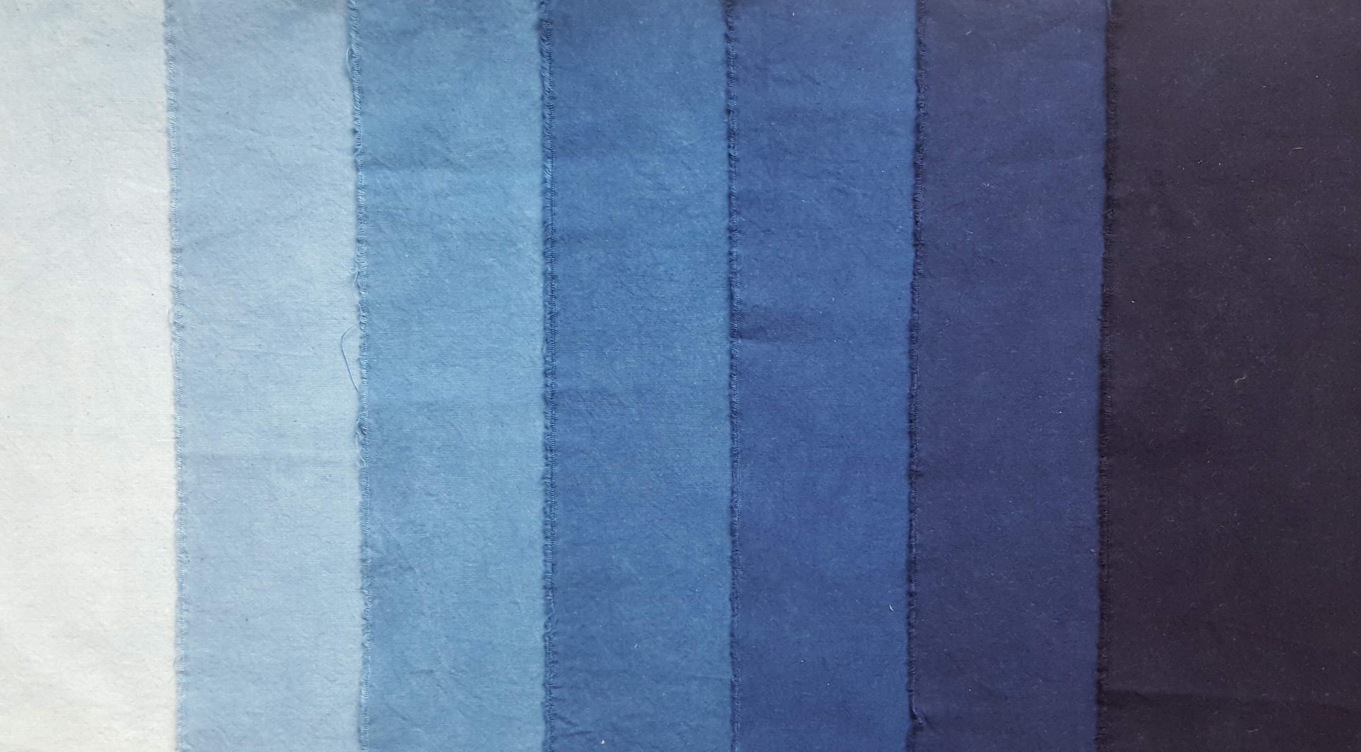 Seven swatches of blue fabric from very pale on the left to dark navy blue on the right