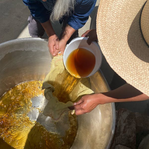 Pouring orange liquid through cheesecloth into a large metal pot