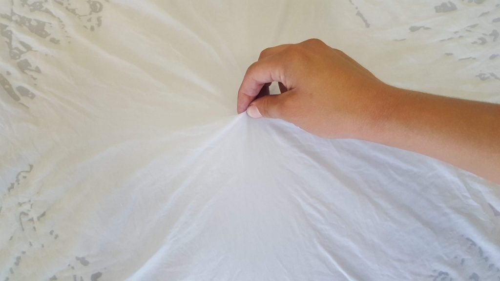 a hand picking up the center of a piece of white fabric
