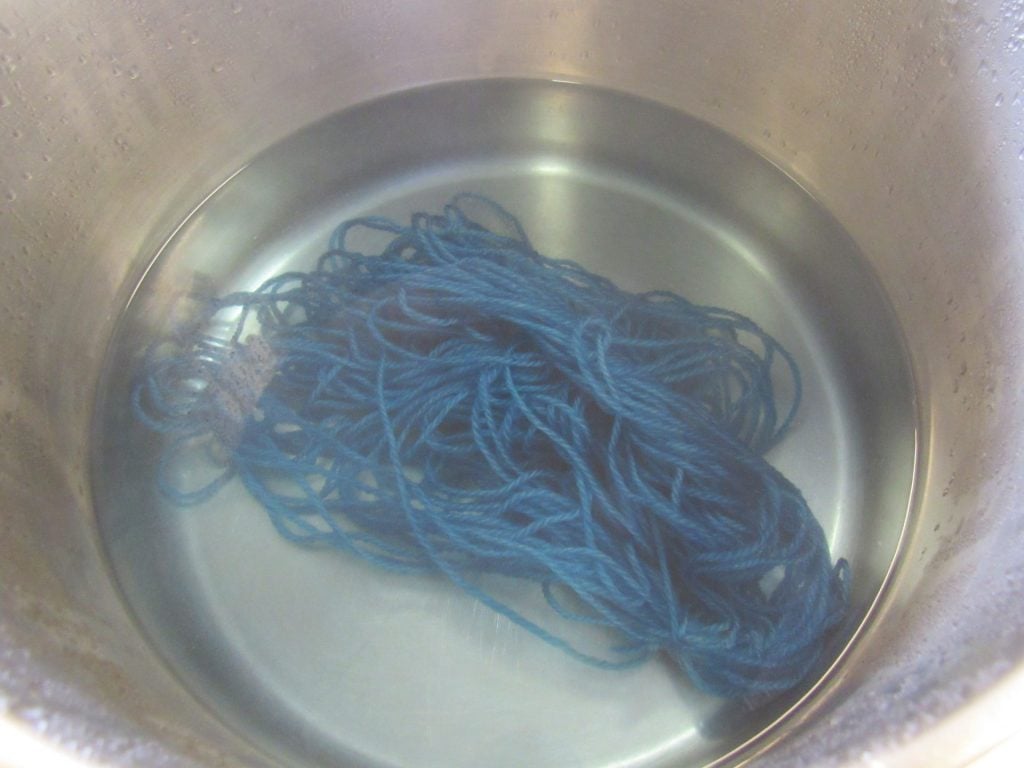 blue skein of yarn in an exhausted dyebath that is almost clear