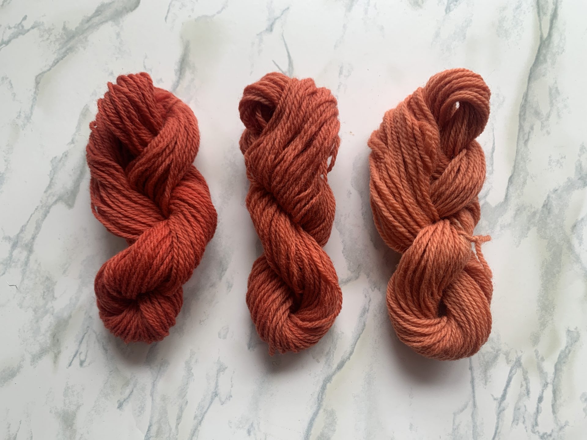 Three red and pink skeins of yarn on a marble background.