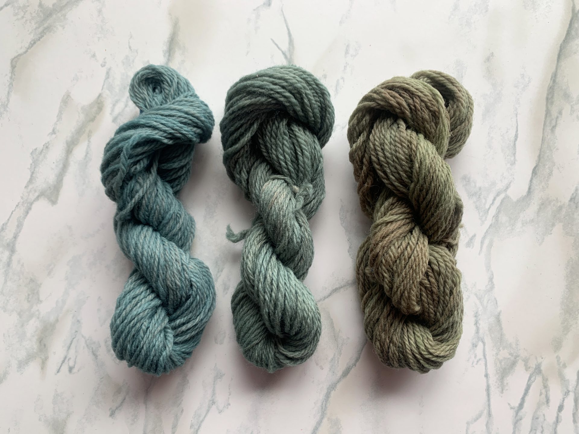 three skeins of blue and gray yarns on a marble background