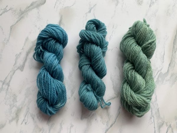 three skeins of blue and green yarns on a marble background