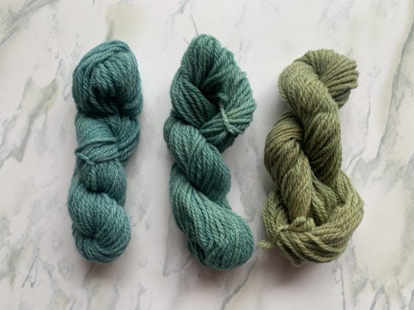 three skeins of blue and green yarn on a marble background