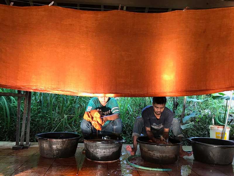 two people squatting behind dye pots with a large pieces of fabric suspended above them