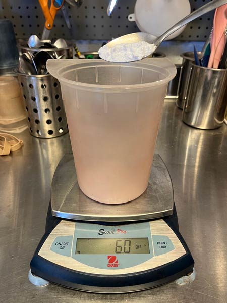 measuring a white powder into a plastic beaker with a spoon
