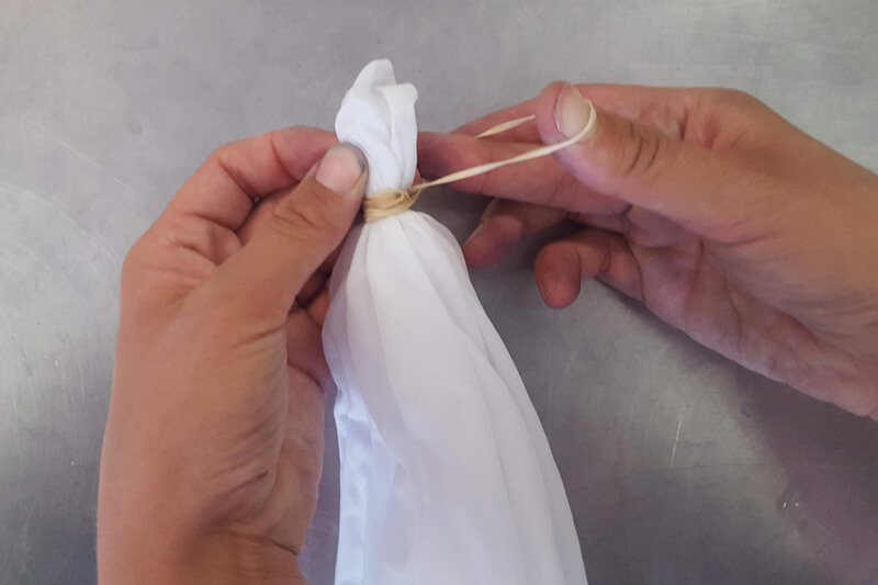 hands wrapping a rubber band around white fabric