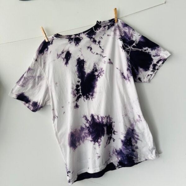 Shibori dyed logwood purple organic mordanted t-shirt facing forward and hanging from a clothesline from two clothespins