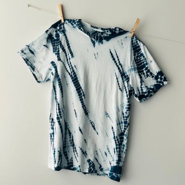 Indigo dyed shibori mordanted organic t-shirt is hanging facing front against a white wall. It is pinned to a clothesline with wooden clothespins